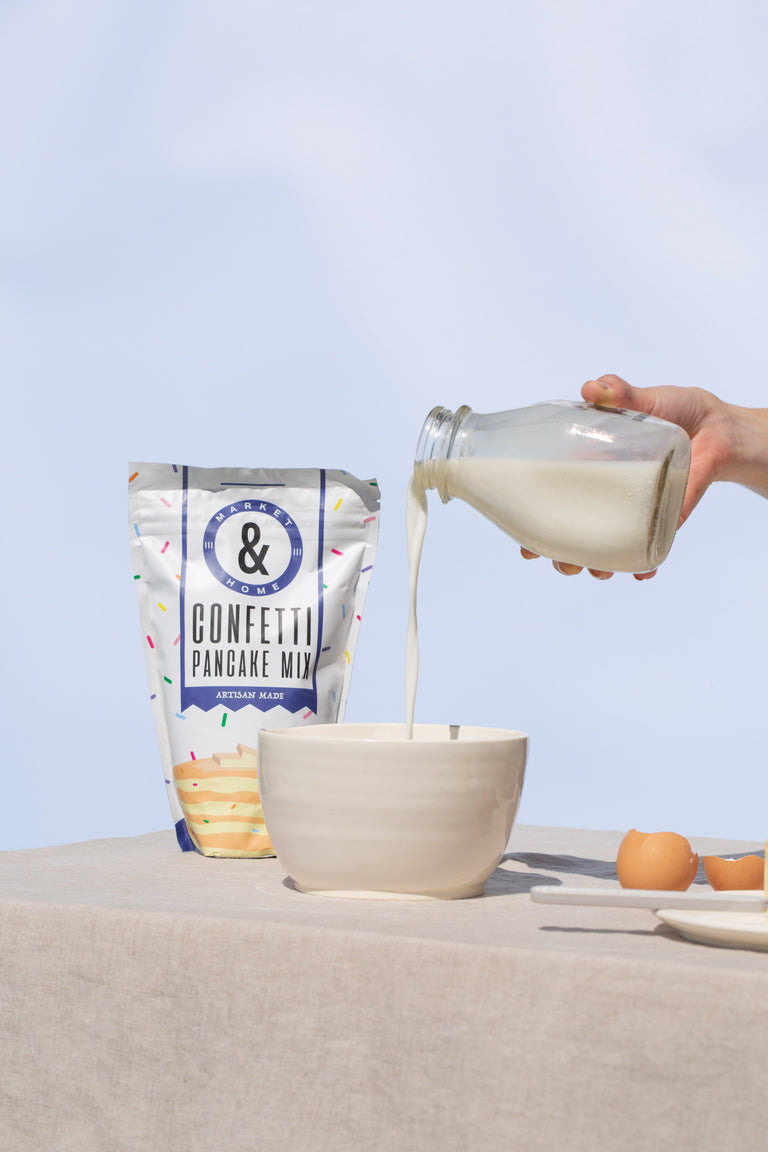 Milk being poured into a large ceramic mixing bowl with large confetti pancake mix